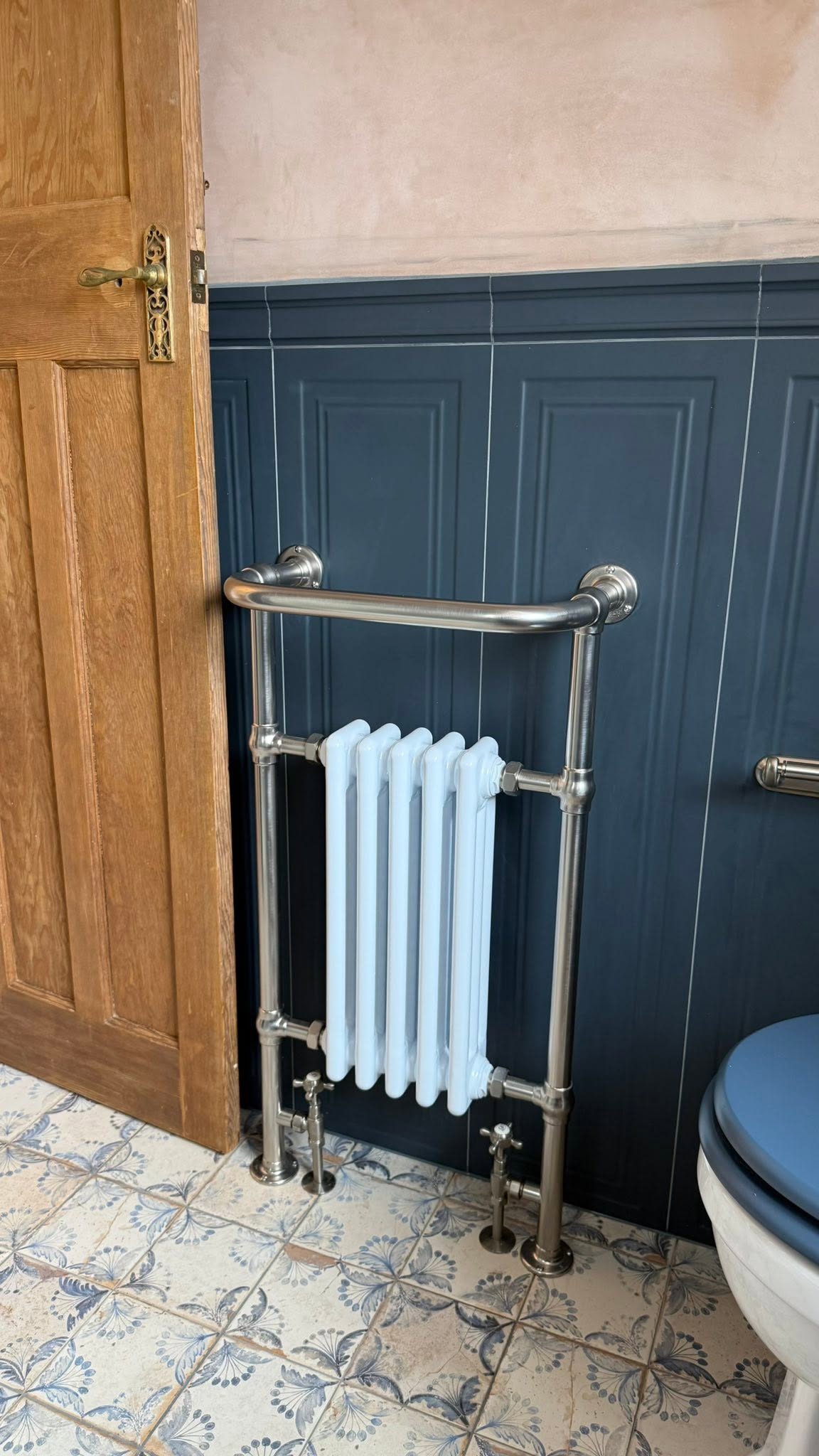 Traditional towel radiator against navy panelling above patterned floor tiles