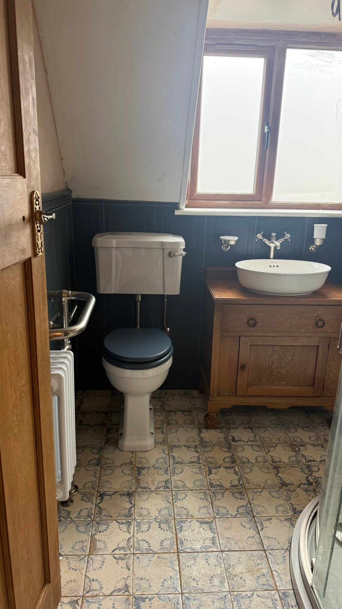 Bathroom with a wooden washstand, vessel basin and blue toilet seat under a sloping ceiling
