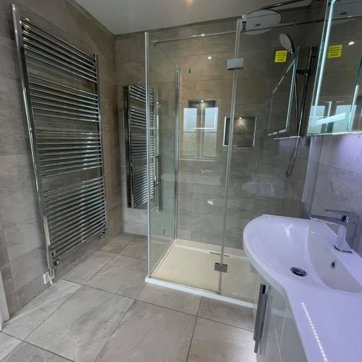 Grey-tiled shower room with a frameless glass enclosure and a tall chrome towel rail
