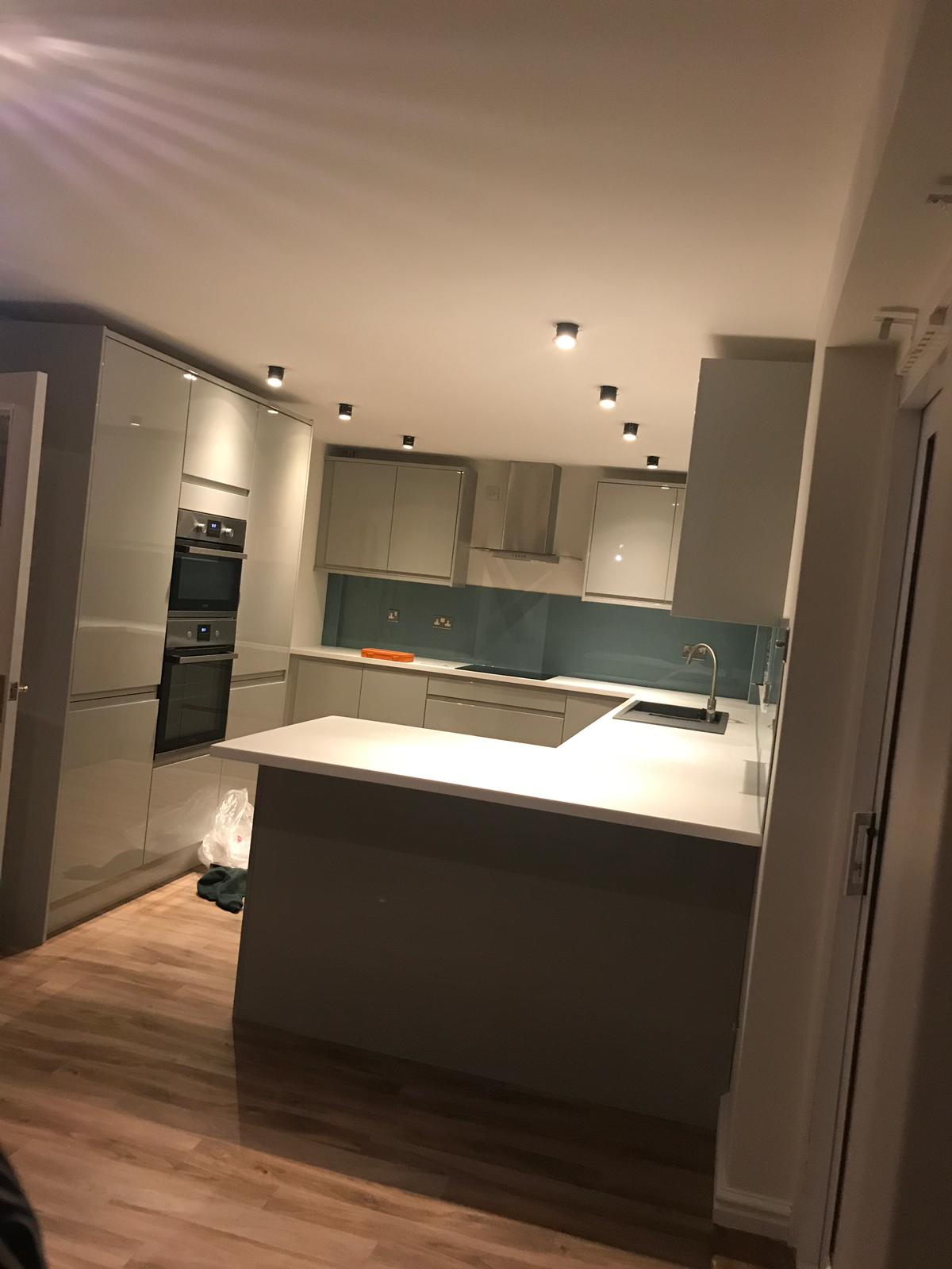 Handleless grey gloss kitchen with a peninsula and a blue glass splashback