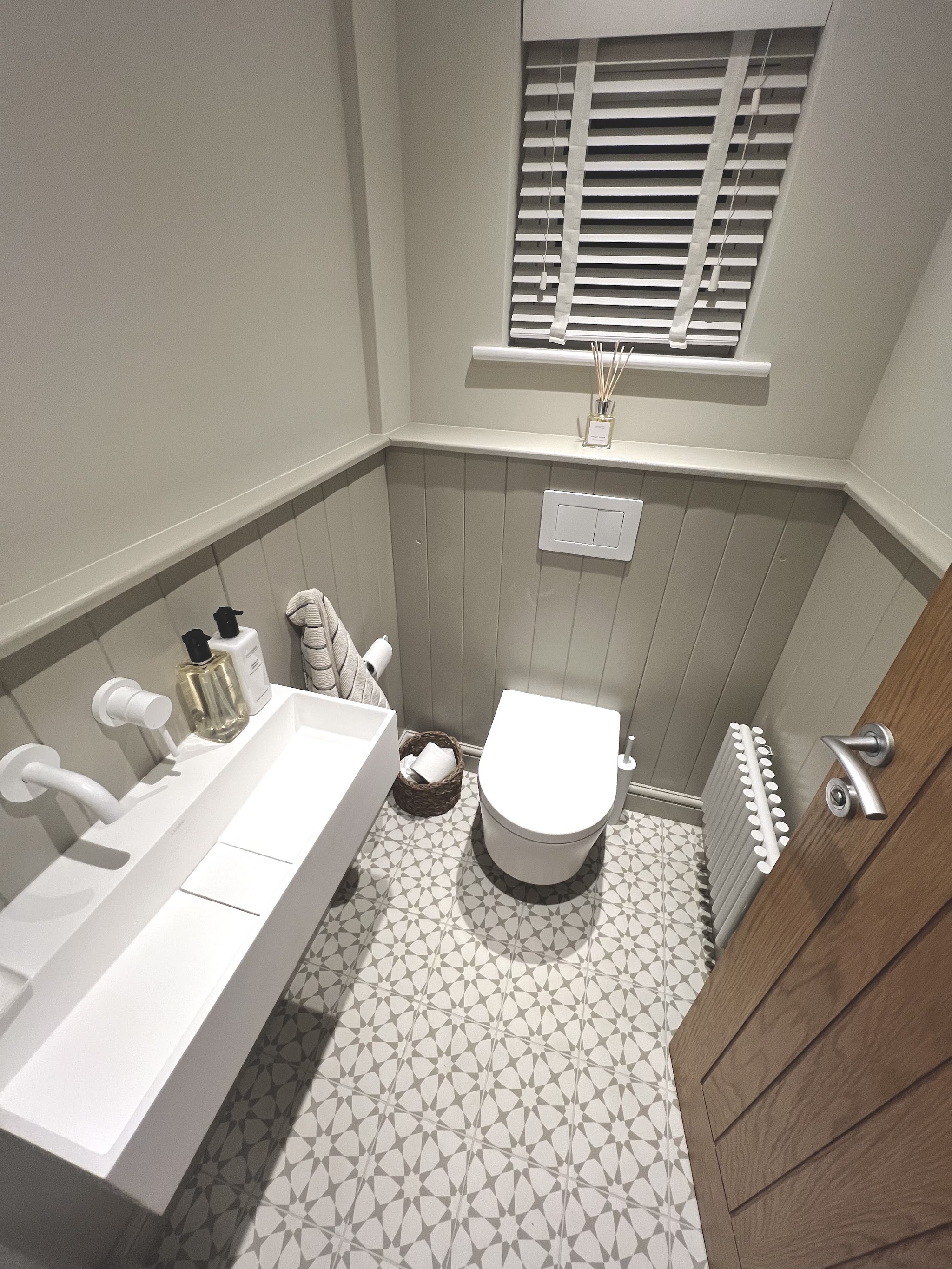 Downstairs cloakroom with grey panelling, a wall-hung toilet, a trough basin and patterned floor tiles